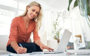 Smiling woman looking at laptop and writing in notebook