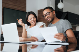 Young couple sitting at a table looking at important papers with a laptop open