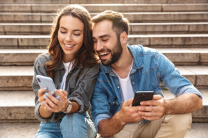 Young couple sitting together on stairs looking at each other phones