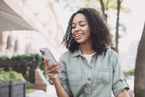 Woman smiling while looking at her phone outside