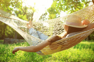 A person relaxing in a hammock outdoors, bathed in sunlight, surrounded by lush greenery.