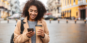 Young woman smiling at phone holding coffee