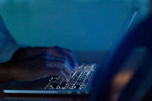 Person's typing on a laptop in a dark room.