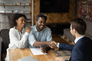 Happy young couple shaking hands with a banking advisor. The desk has a contract on it.